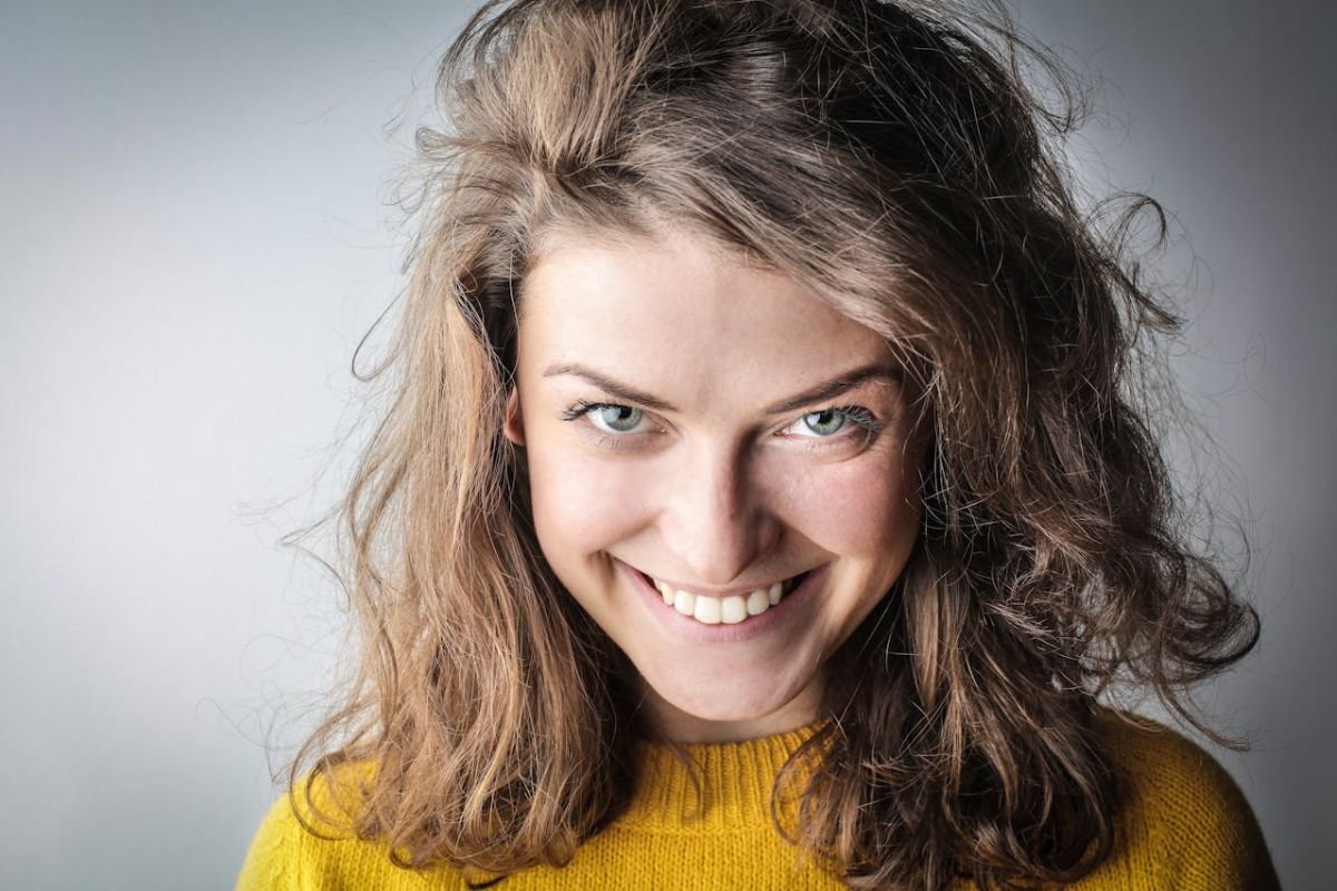 The Mask of Kindness: A Disarming Grin Close-up portrait of a woman in a yellow sweater with an unsettling grin, looking directly at the camera.
