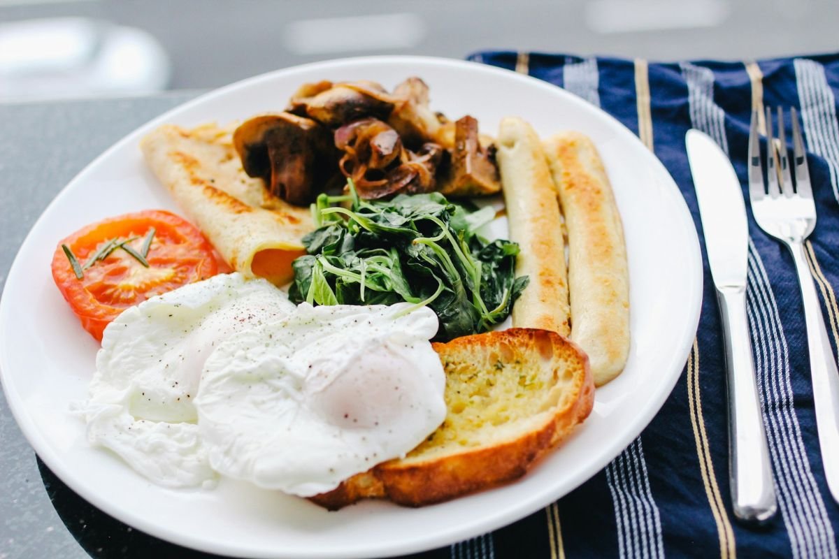 Classic Breakfast Pairings with Poached Eggs A breakfast plate featuring poached eggs, grilled tomato, sautéed mushrooms, greens, toasted bread, and sausages.
