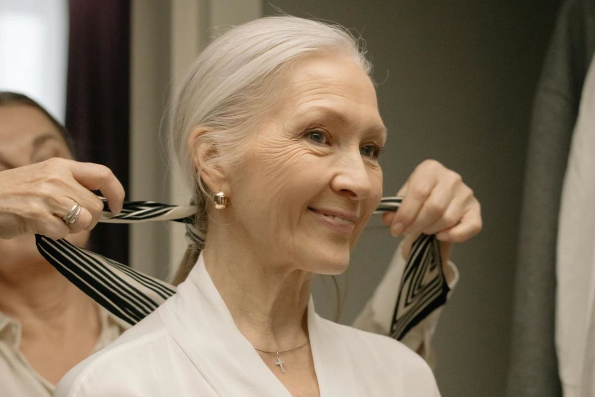 Embracing Aging Gracefully: A Warm Smile from Within A serene older woman in a white robe smiling warmly, seated in a cosy indoor setting with soft natural light.