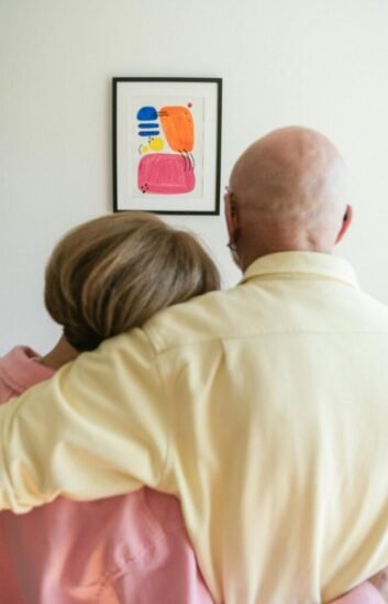An older couple embraces while admiring a piece of artwork, reflecting a lifetime of shared experiences and deep connection.
