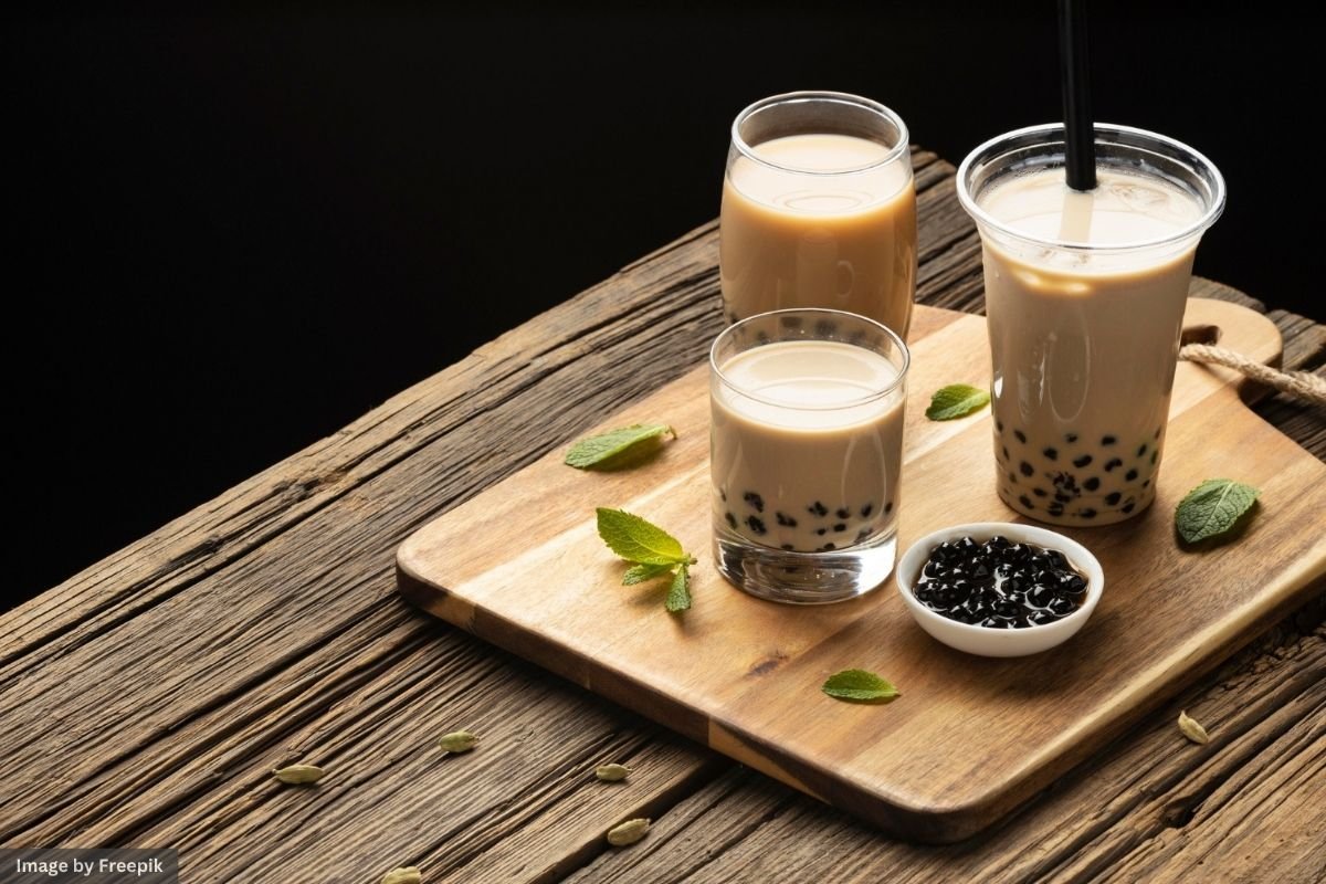 A tall glass of bubble tea with a straw, surrounded by tapioca pearls, set on a wooden surface.