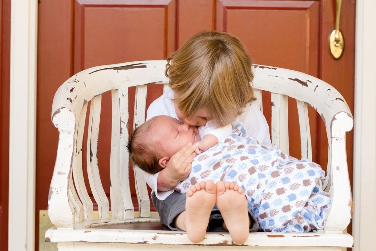 Young boy gently holding and kissing a baby sibling, showing care and affection.