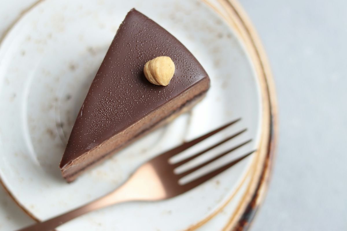 Chocolate Mousse Cake with Hazelnut A slice of chocolate mousse cake topped with a single hazelnut, served on a white ceramic plate with a copper fork.