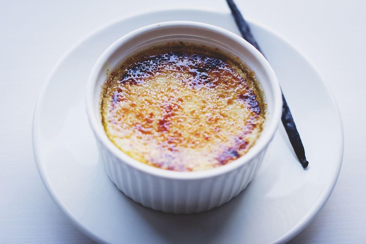 Golden Crème Brûlée A white ramekin filled with golden-brown caramelised crème brûlée placed on a white plate, with a vanilla bean garnish on the side.