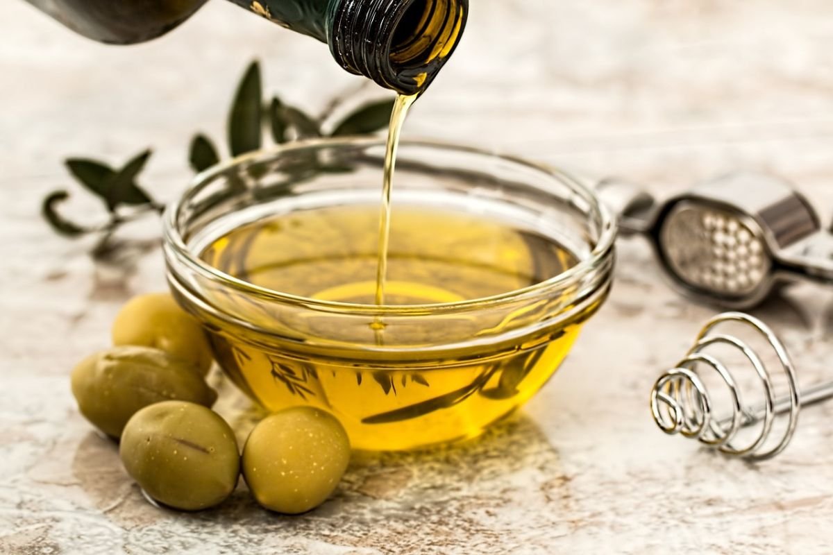 Extra Virgin Olive Oil: Liquid Gold for Health and Flavour Fresh olives with a bottle of golden olive oil on a rustic wooden background.