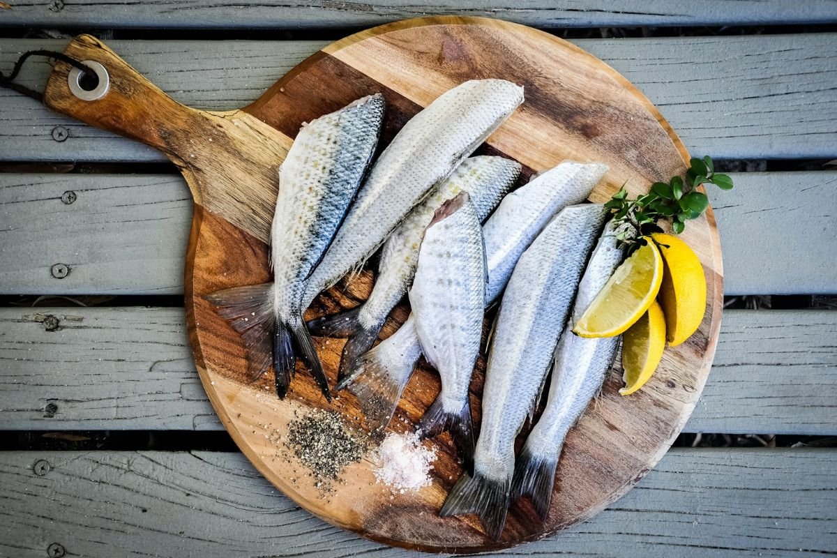 Headless white fish with lemon slices on a wooden chopping board.