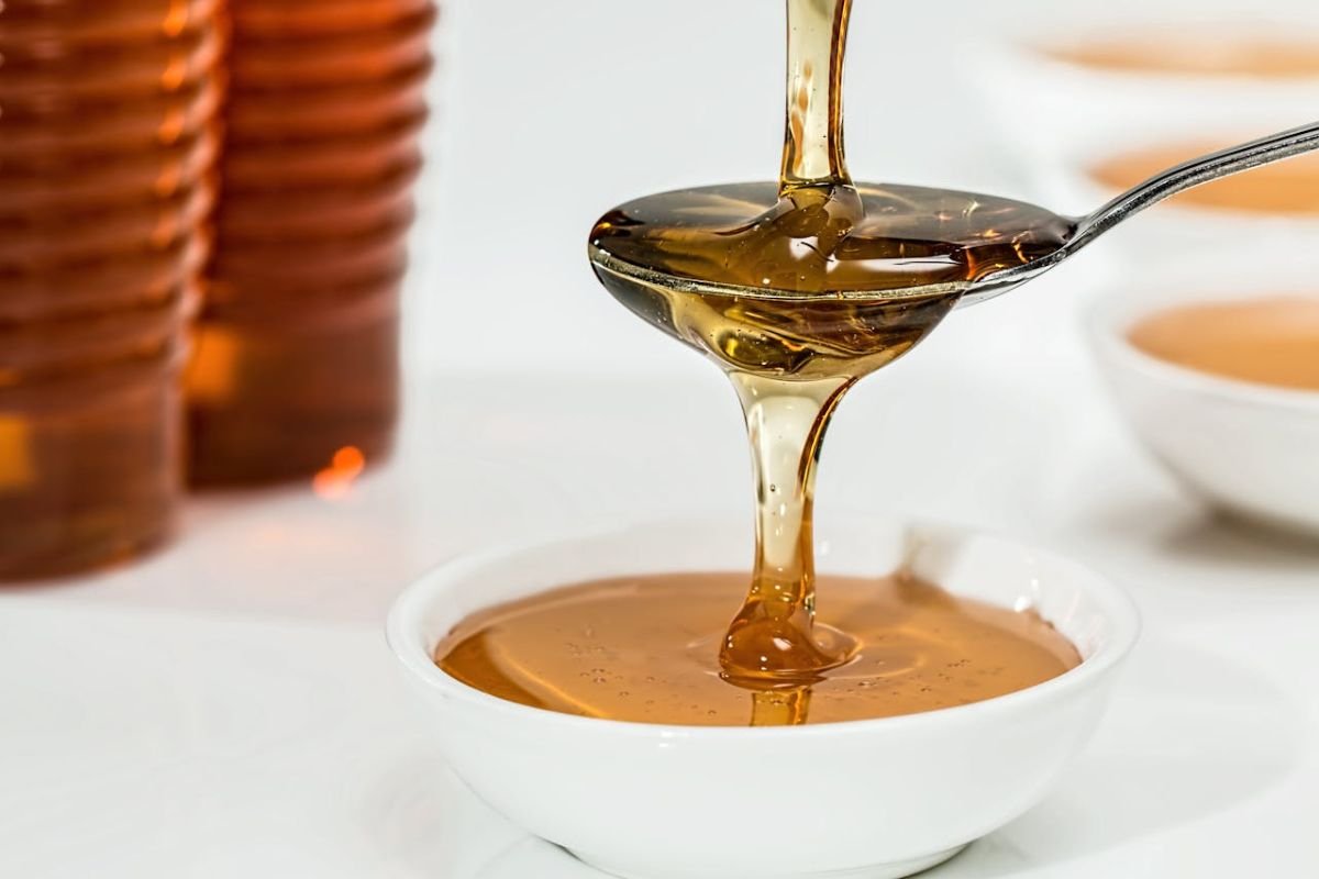 Golden honey drizzling into a white bowl on a wooden surface.