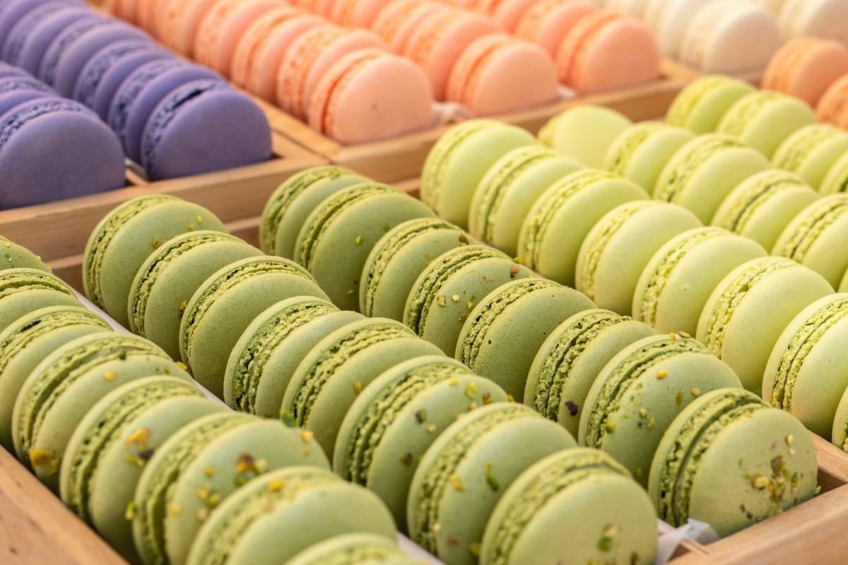 Assorted Macarons in Wooden Trays Rows of colourful macarons in green, pink, and purple arranged neatly in wooden trays.