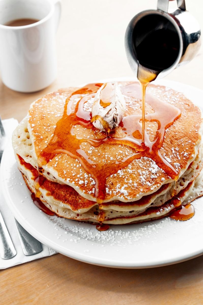 Sweet Temptation: What’s Really in Your Syrup? Stack of golden pancakes with syrup being drizzled over the top, capturing a warm and delicious breakfast moment.