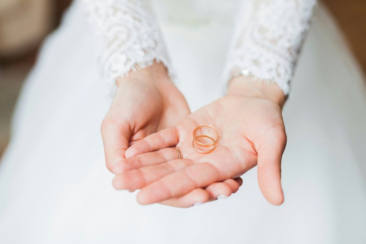 A Bride’s Promise: Holding the Symbols of Commitment A bride in a white wedding dress holds two gold wedding rings in her open palms, symbolising the beginning of a lifelong commitment.