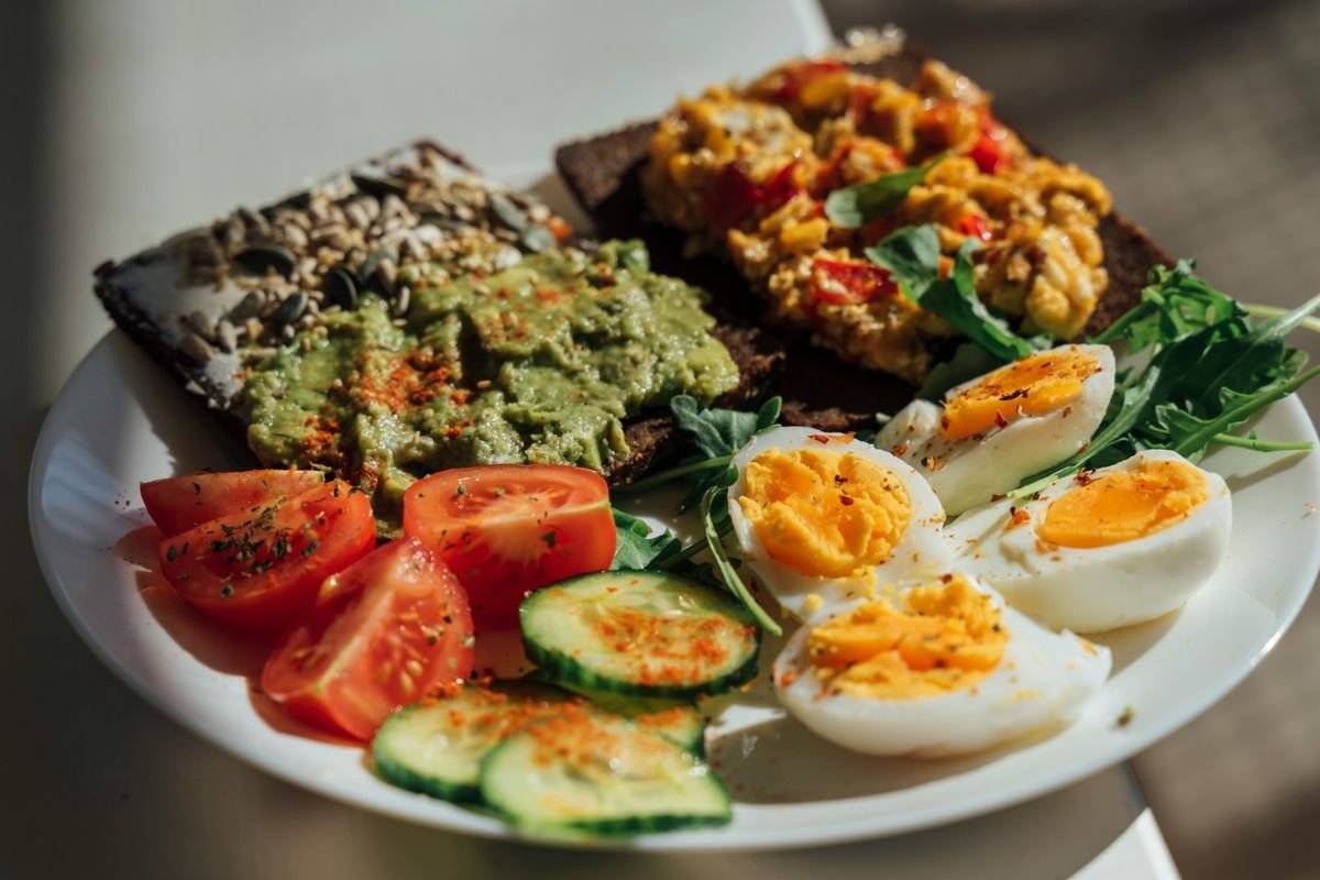 A healthy plate of avocado toast, eggs, tomatoes, and cucumbers garnished with herbs.