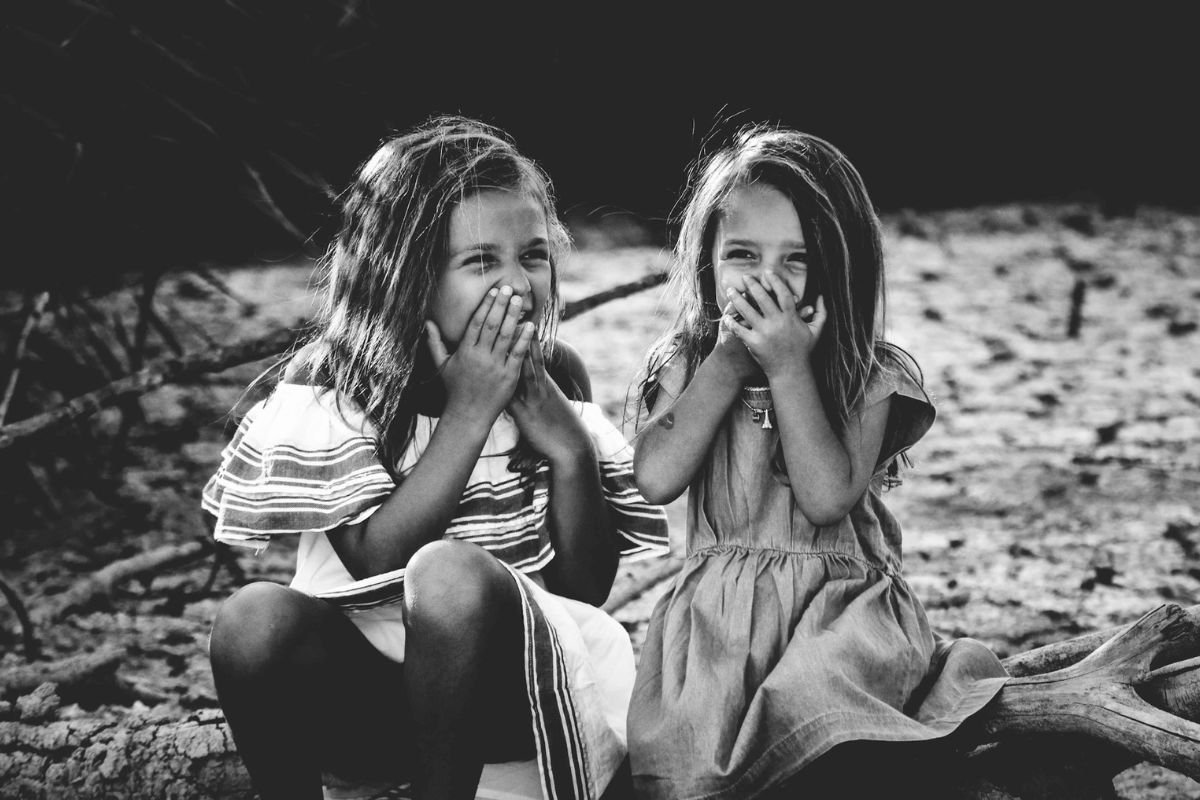 Two young girls in a grayscale image sharing a playful moment.