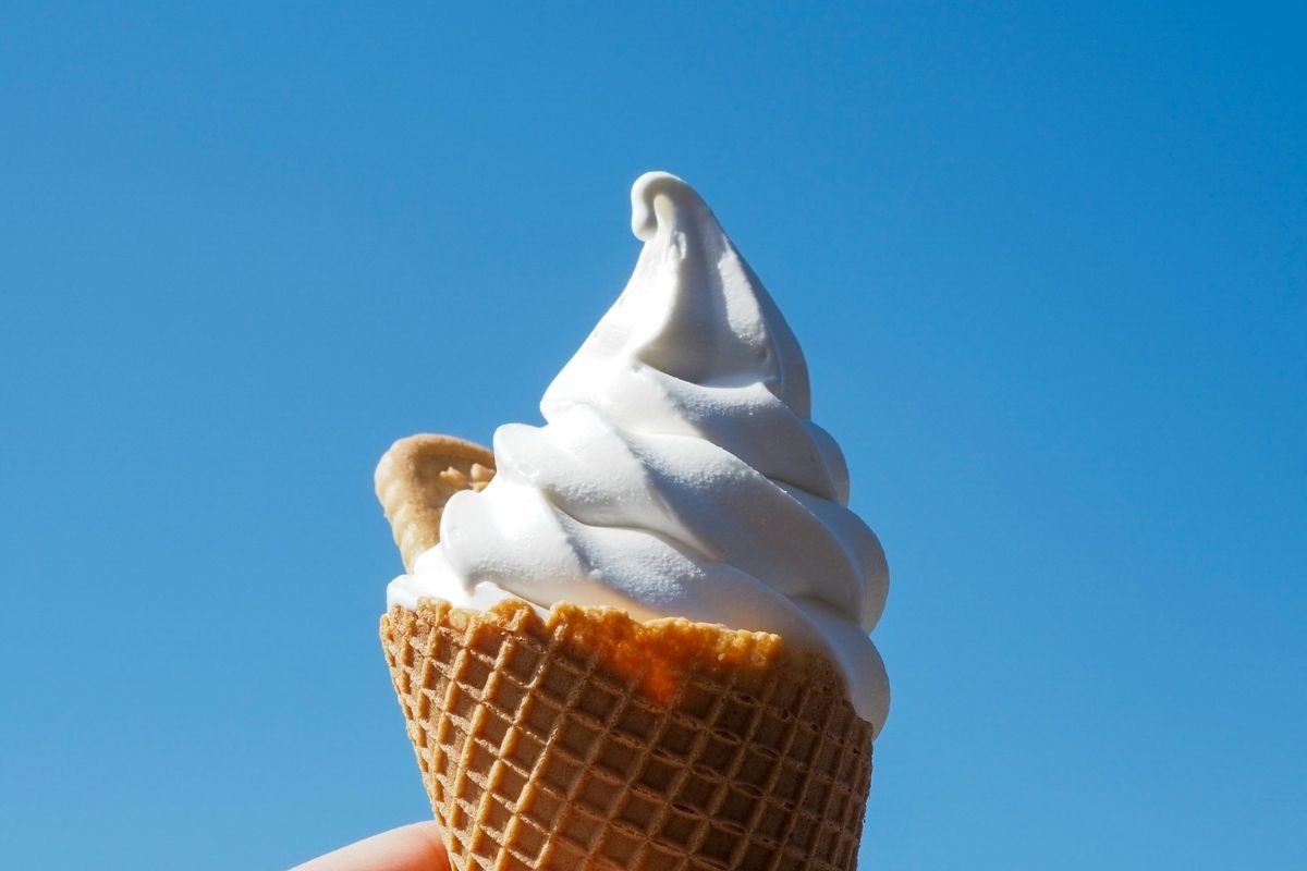 Vanilla Soft Serve Cone on a Sunny Day A vanilla soft serve ice cream cone held against a clear blue sky.