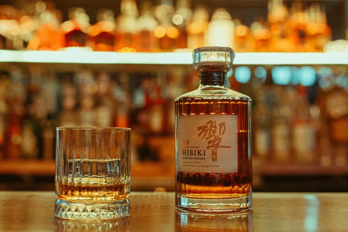 A bottle of whisky next to a glass of poured whisky on a wooden surface.