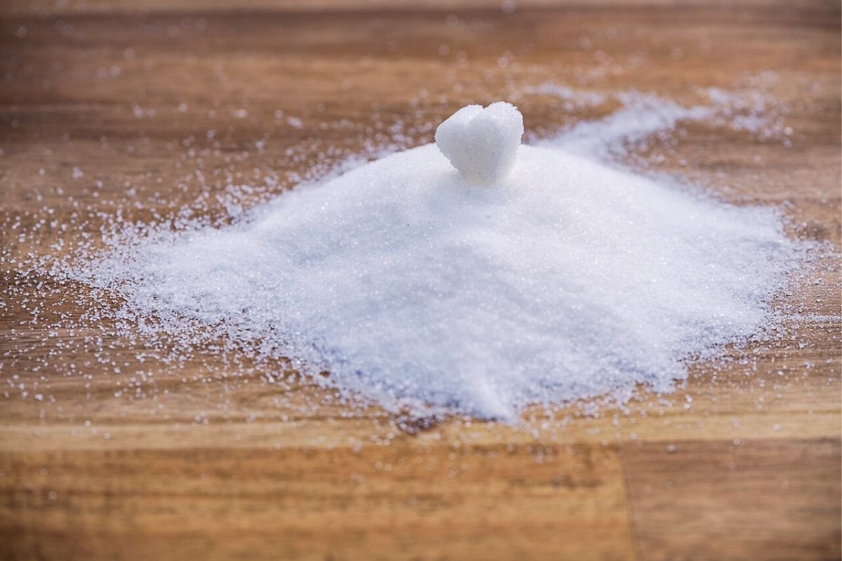 Sugar Pile with Heart-Shaped Cube A pile of white sugar with a heart-shaped sugar cube on top, scattered slightly on a wooden surface.