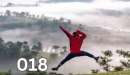 A young man jumping joyfully on a grassy hill under a clear blue sky, symbolising freedom and happiness in solitude.