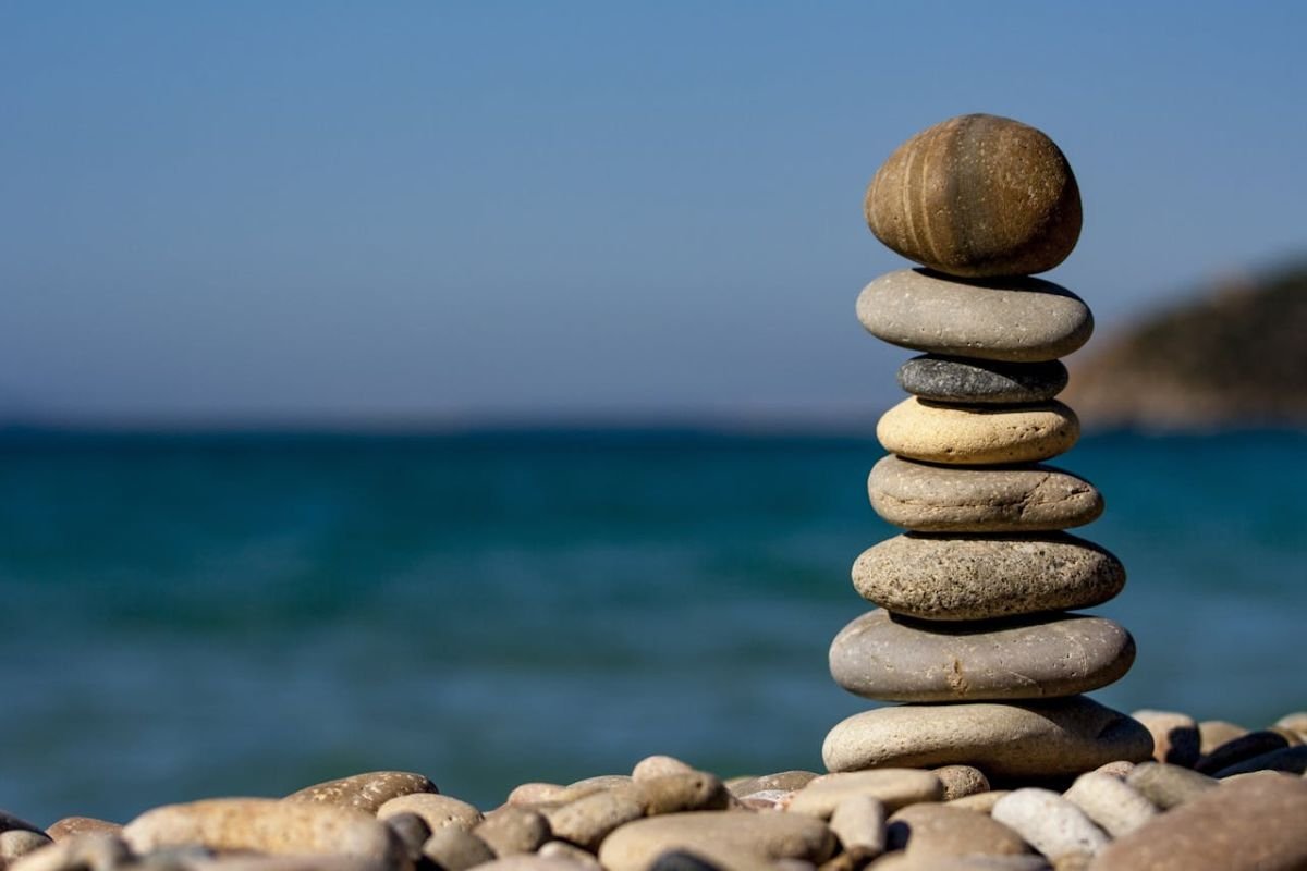 Cairn Stones by the Water: A Symbol of Patience and Perseverance A stack of cairn stones on a shoreline, symbolising patience, balance, and resilience against mental exhaustion.