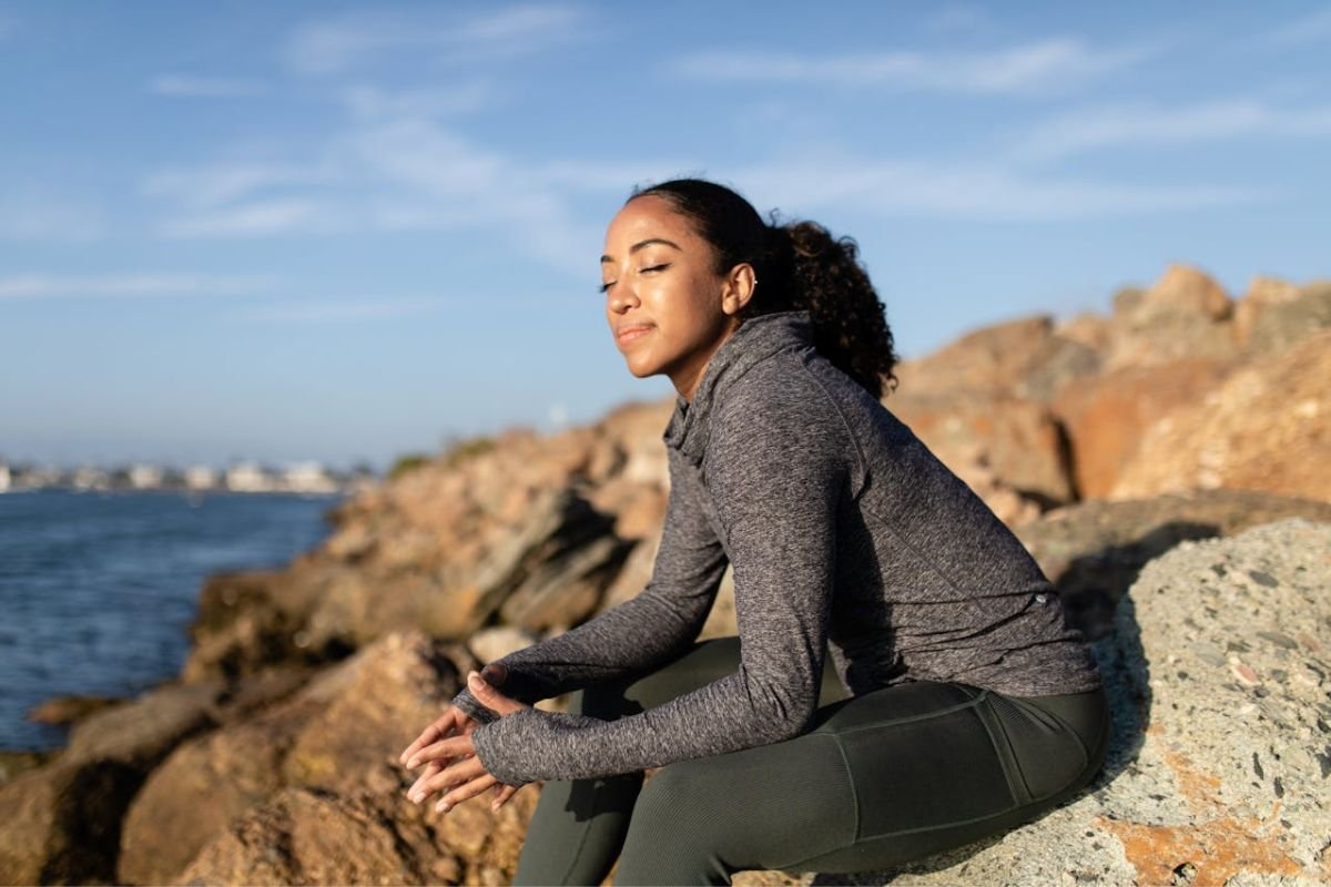 Woman Sitting in Calm Reflection After Mental Clarity Woman sitting on a rock, gazing into the distance with a clear, calm expression, symbolising a peaceful mind.