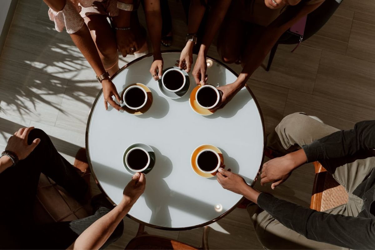 A round table with five cups of coffee and five people gathered around, symbolising social interactions often deemed unnecessary.