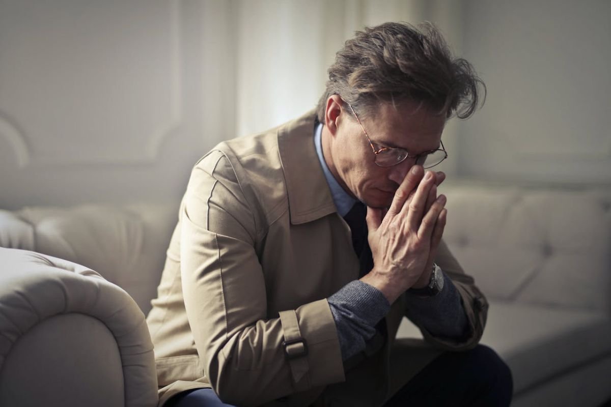 Businessman Struggling with Mental Exhaustion A mature businessman sits with his hand on his chin, looking distressed and mentally exhausted.