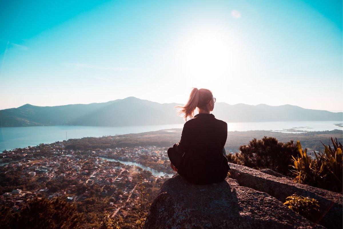 A woman sitting at the edge of a mountain cliff, gazing into the vast landscape, reflecting peace and mindfulness in solitude.