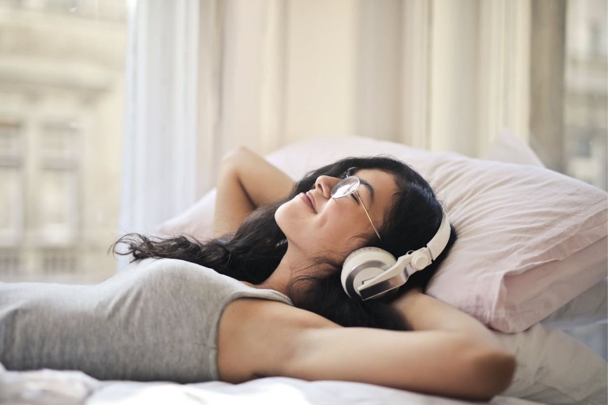 A woman lying on her bed, smiling while listening to music, symbolising the joy of solitude and freedom from energy-draining relationships.