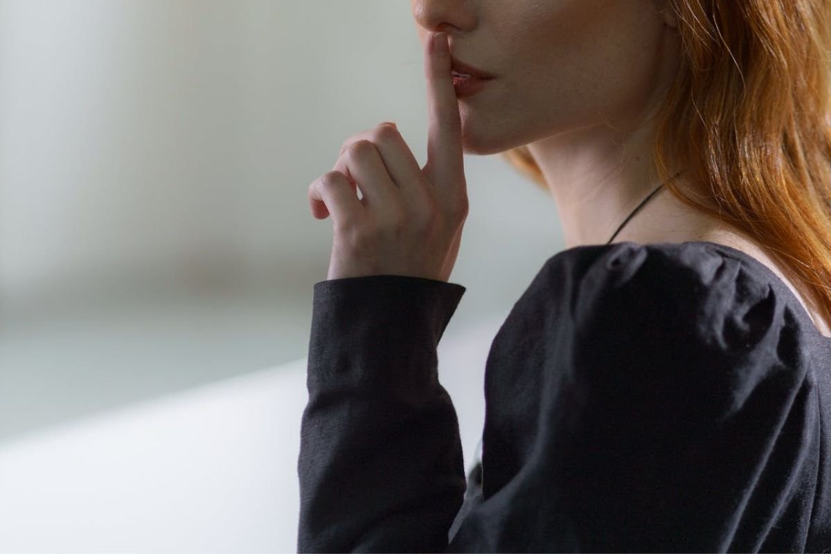 The Power of Quiet: Why Some Family Matters Should Stay Private A woman in a black top holding her finger to her lips, symbolising quietness and the importance of keeping family secrets private.