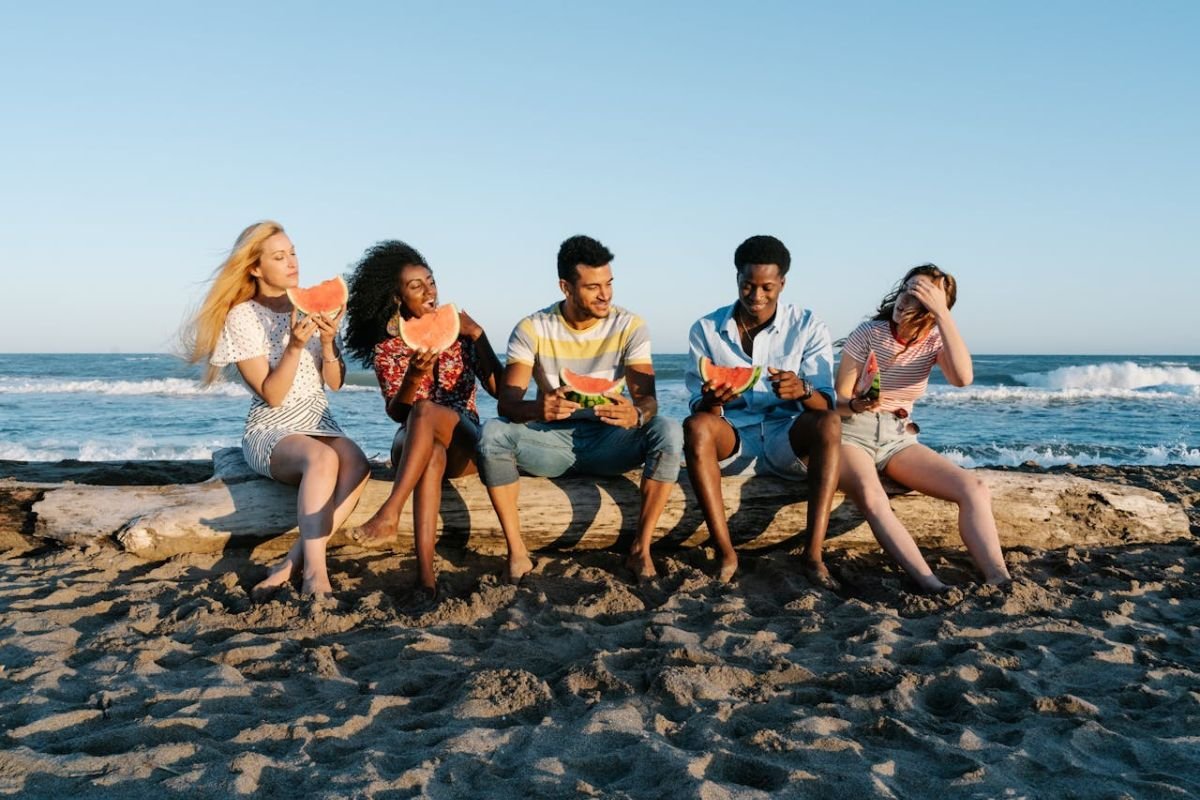 Cherishing Life’s Companions: Friends Sharing Watermelon on the Beach Five diverse friends sharing watermelon slices on a sunny beach, enjoying laughter and meaningful connections.