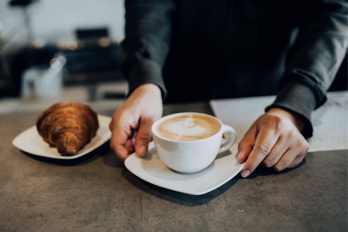 Hands Serving Coffee and Pastry: A Story of Selflessness and Sacrifice Hands serving a coffee cup and croissant pastry, symbolising the elder brother’s selflessness and sacrifice in the story of the two brothers.