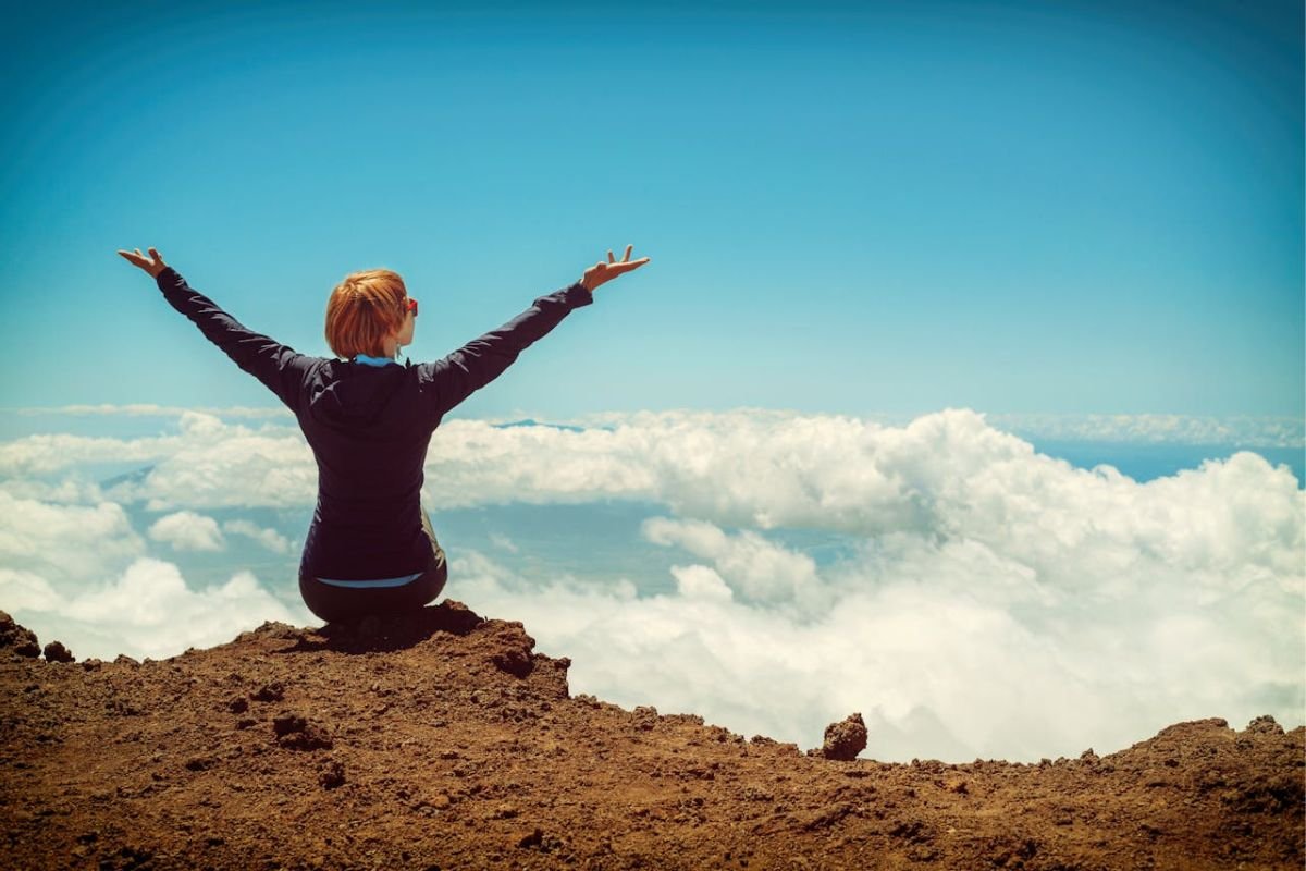 A person sitting on a cliff with raised hands, symbolising emotional freedom and the saying "Ignorance is Bliss."