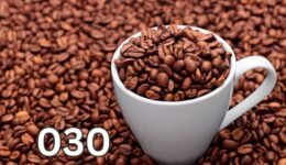A close-up of a ceramic mug filled with coffee beans, surrounded by scattered beans on a rustic wooden surface.