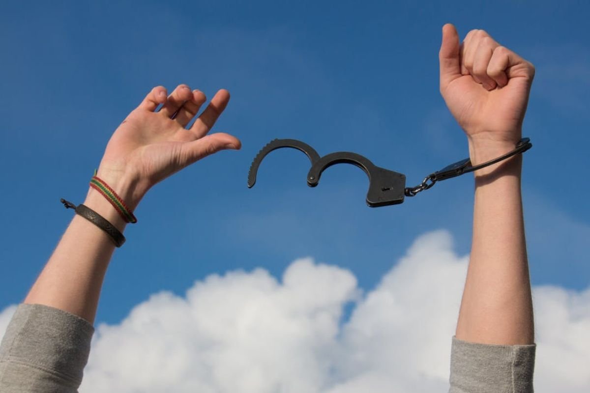 A person’s arms raised into the sky, breaking free from handcuffs, symbolising the liberation from limiting beliefs and the poverty mindset.