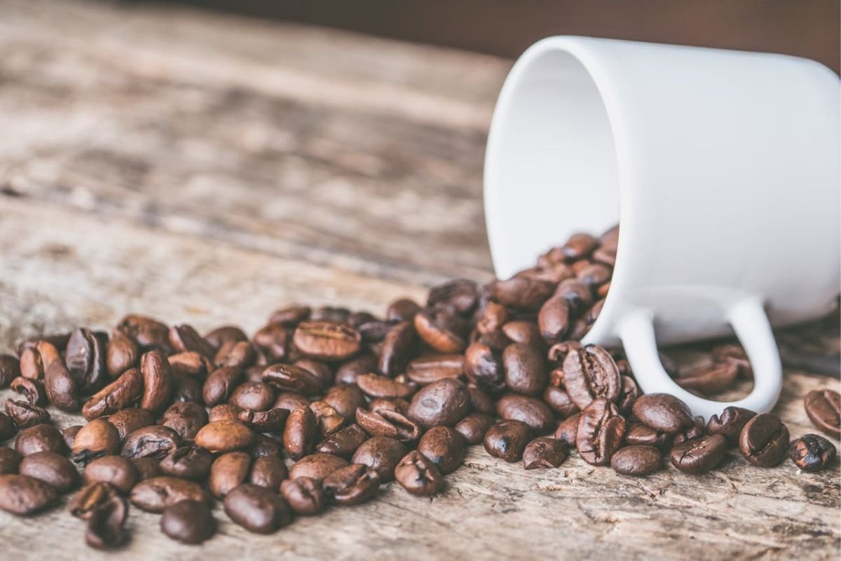 Spilled Coffee Beans: A Symbol of the Coffee Crisis A white mug tipped over with spilled coffee beans on a wooden surface, symbolising the ongoing coffee production crisis.