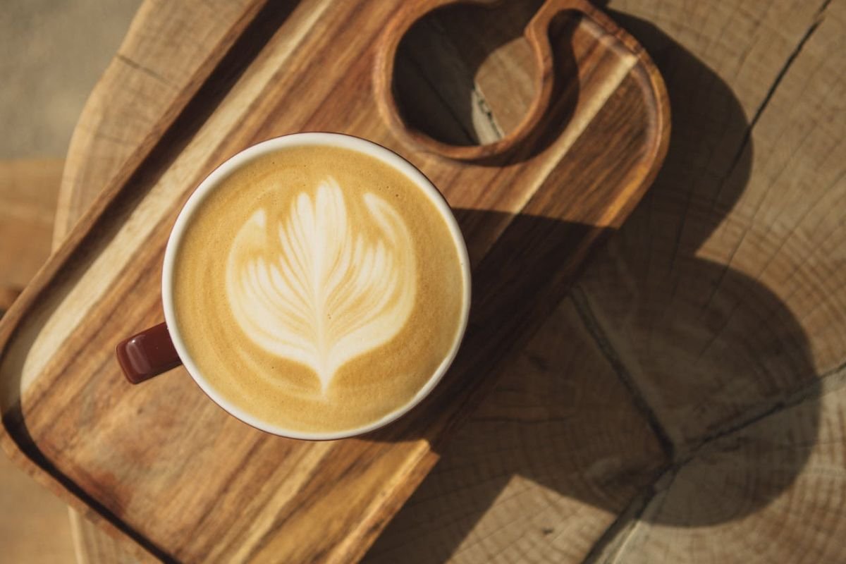 A beautifully crafted latte with a leaf-shaped pattern, served on a wooden tray with a serene coffeehouse ambiance.