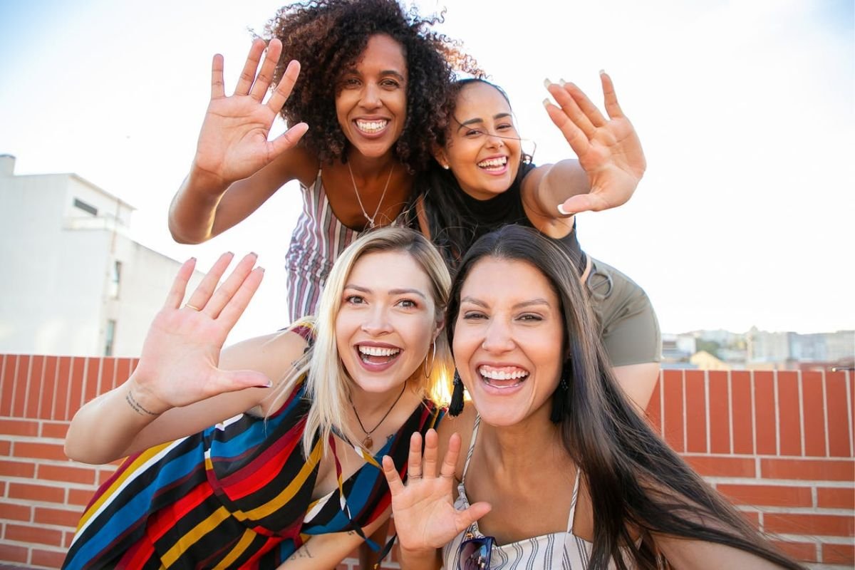 A group of women smiling and raising their hands with open palms, symbolising trust, transparency, and openness in communication.