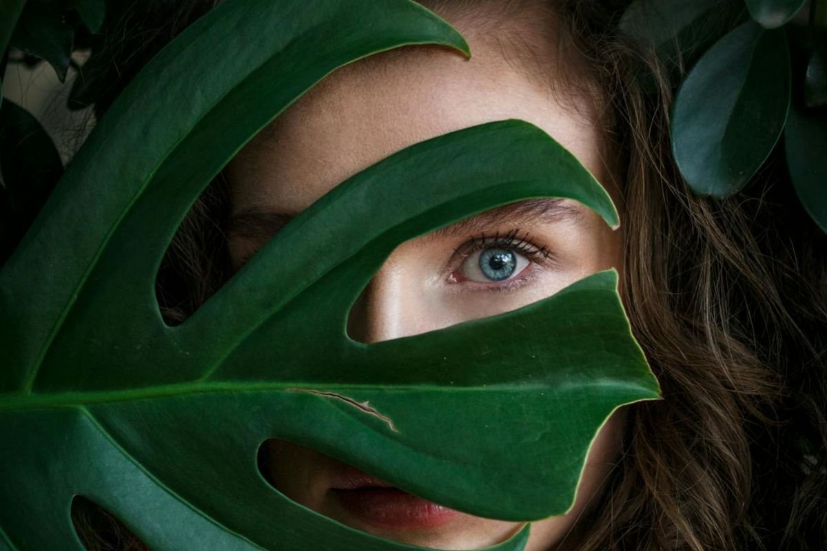 Unlocking Secrets: The Power of Eye Movements in Body Language A woman covers one eye with a green leaf, leaving the other eye visible, symbolising the mystery of uncovering thoughts through body language.