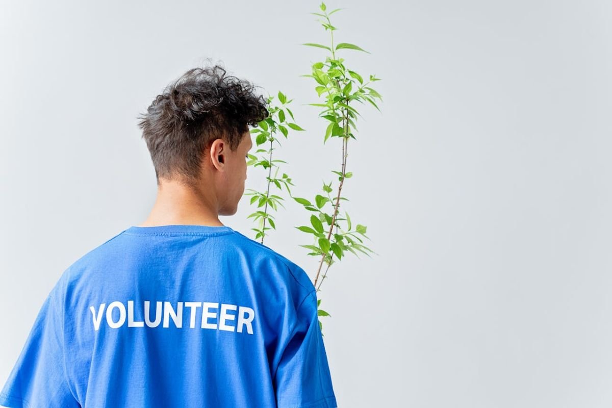 A person wearing a ‘volunteer’ shirt holding a green plant, symbolising the connection between generosity, creating value, and long-term wealth-building.