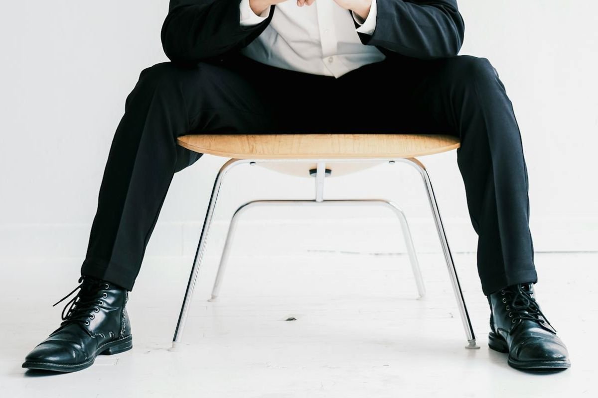 Confidence in Posture: What Sitting with Legs Apart Reveals A person seated in a minimalist setting with legs apart, subtly communicating confidence and readiness through an open-legged posture.