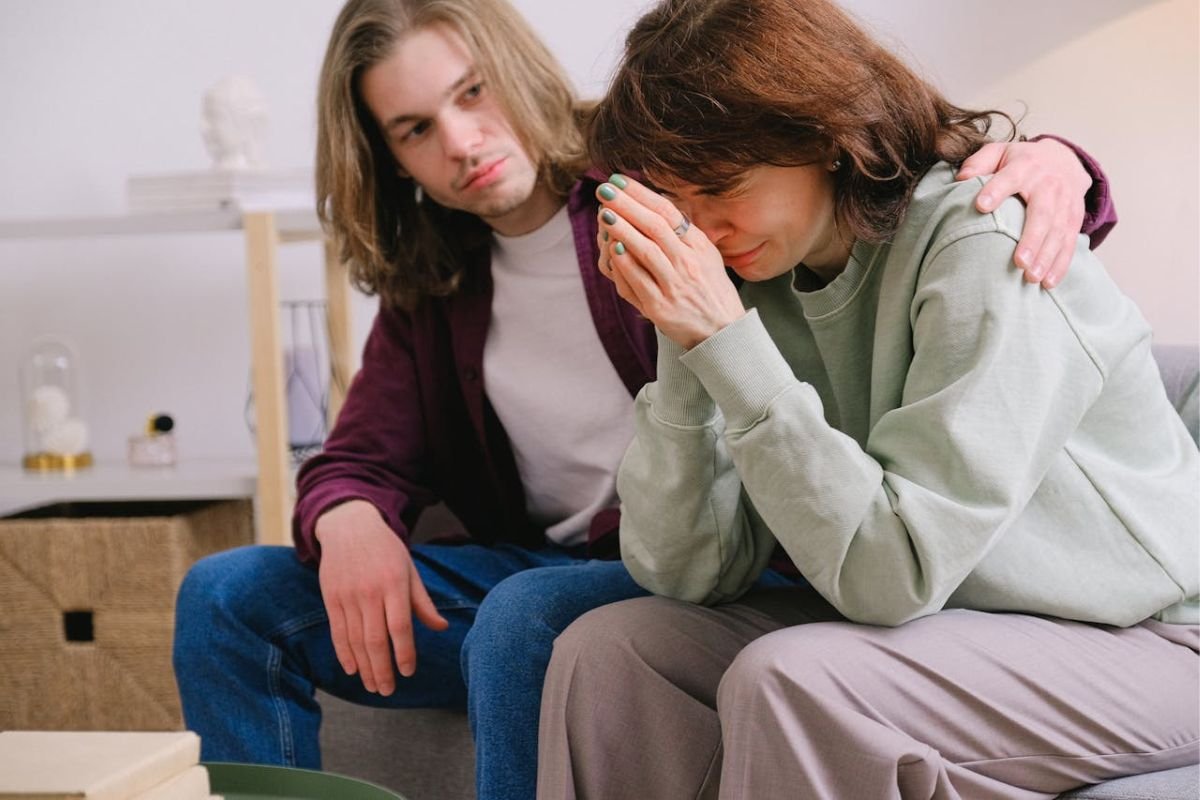 Absorbing Emotions: The Silent Weight of an Empath A man sitting beside a crying woman, offering comfort while looking sorrowful, visually representing emotional absorption and deep empathy.