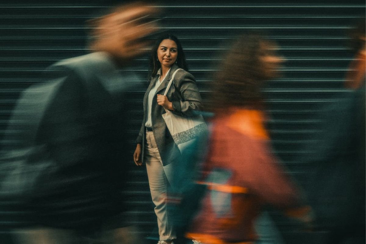 Surrounded by Energy: The Empath’s Experience in a Crowd A woman standing still as people pass by, visually representing an empath absorbing emotional energy from those around her.