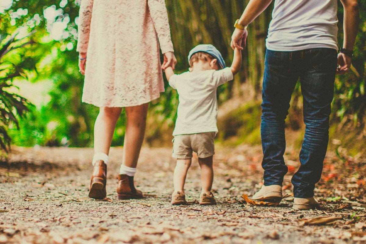 Walking Through Life - Hand in Hand, Heart to Heart A child walks hand in hand with both parents along an unpaved pathway, representing life’s journey and the questions that define our existence.