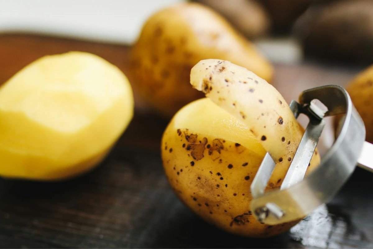 Could You Live on Just Potatoes? Science Says Maybe! A cutting board with a fully peeled potato and another in the process of being peeled, showcasing potatoes as a staple food for survival.