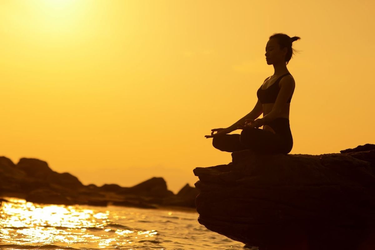 Growth Begins Within: Meditative Stillness and Purposeful Living Silhouette of a woman meditating on a cliff at sunrise, representing inner growth, clarity, and living with true purpose.