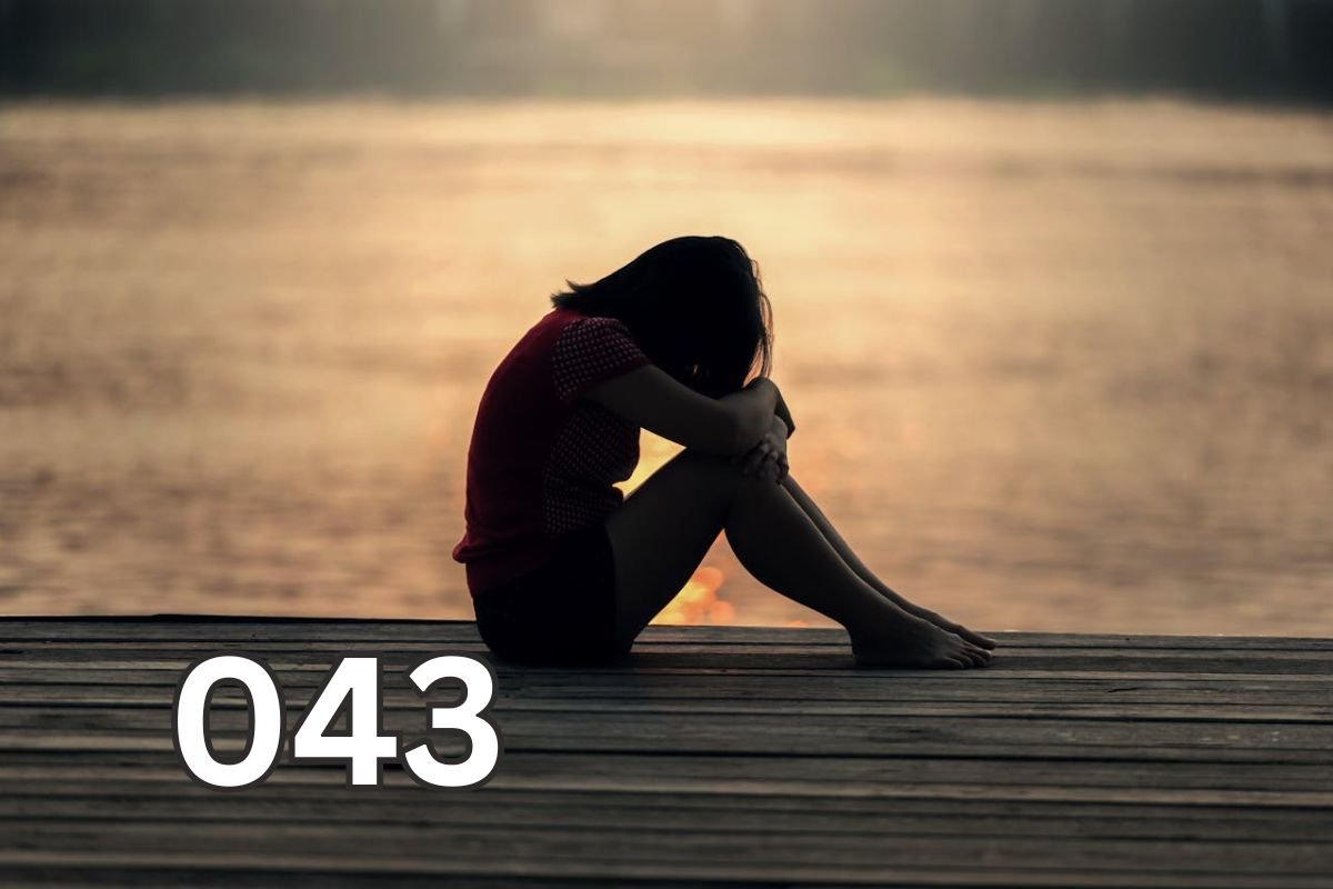 Sad woman sitting alone on a wooden deck, hugging her knees and looking out to sea, symbolising emotional pain and lack of self-love.