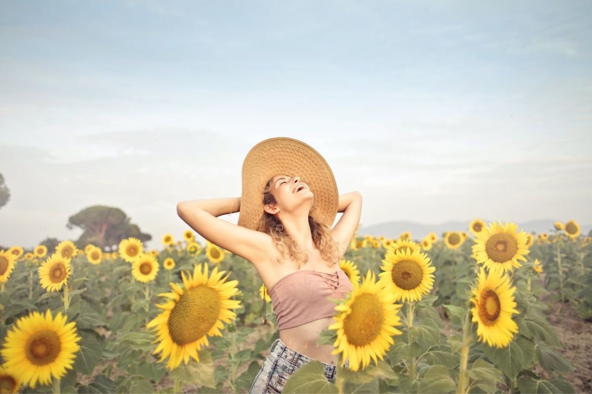 Woman Enjoying Peace in a Field of Sunflowers Happy woman in sunflower field with arms behind head, expressing the peace that comes from a simplified lifestyle.