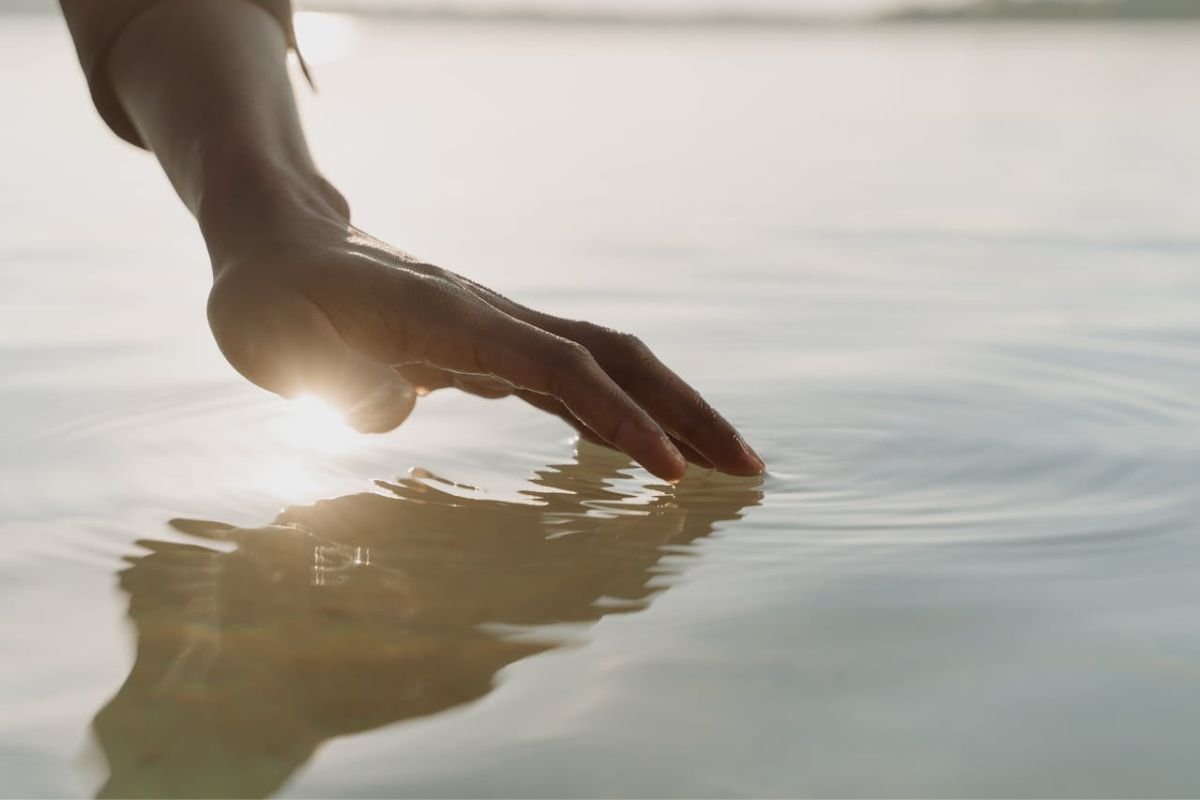 Reaching for Stillness in the Midst of Chaos Hand gently touching calm water, symbolising the pursuit and quiet grasp of peace and mental clarity.