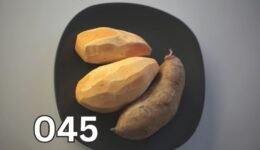Three raw orange-fleshed sweet potatoes placed on a black plate, showcasing their natural texture and earthy tones.
