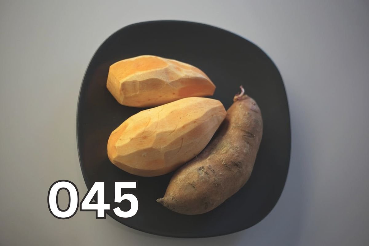 Three raw orange-fleshed sweet potatoes placed on a black plate, showcasing their natural texture and earthy tones.