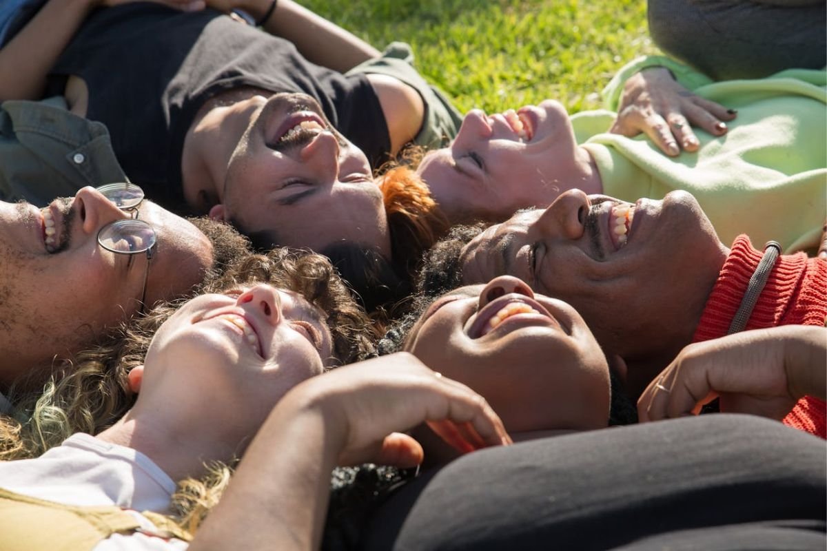 Joy in the Everyday - When You’re Playful, Life Feels Lighter Group of friends laughing on grass field, symbolising joyful living and the magnetic power of humor and playfulness