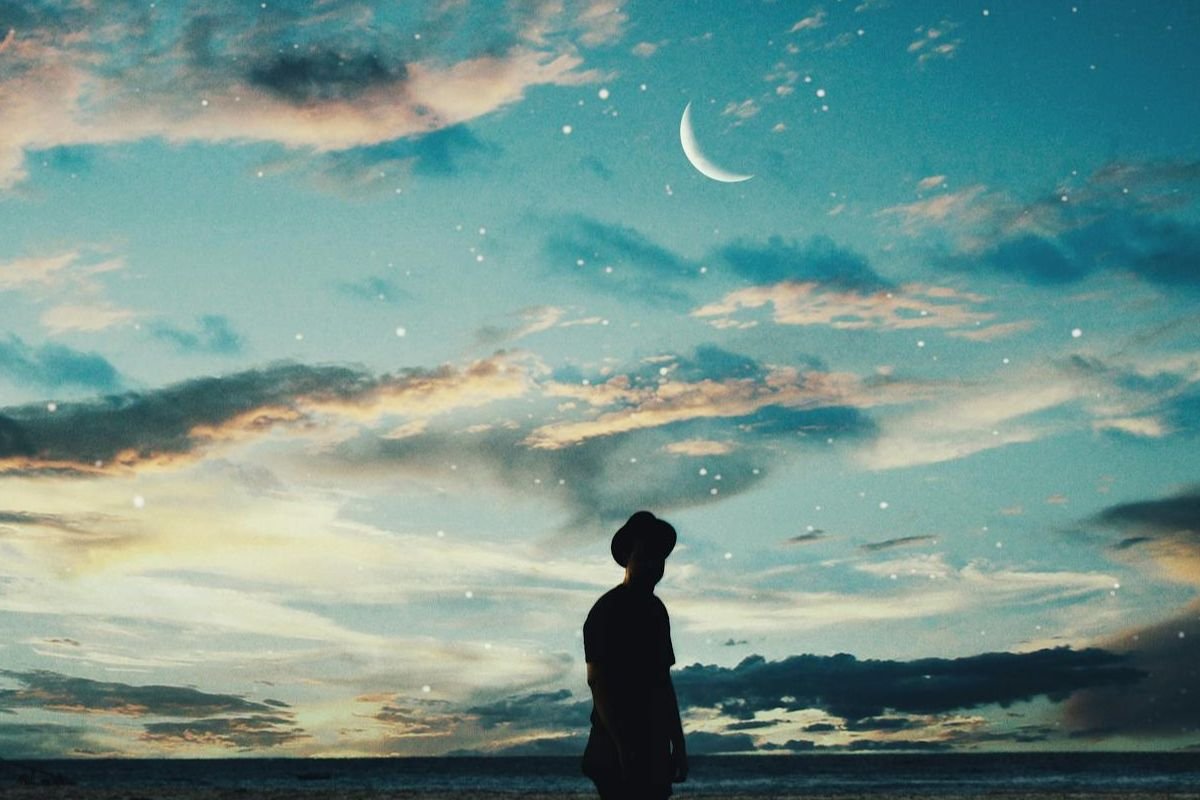 Silhouette of a man standing near water under a starry moonlit sky, evoking the serenity and wonder of lucid dreaming.